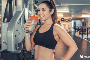 A young fit woman drinks in protein shake in the gym Medifitpro.com